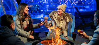 A group of friends by a fire outside of an igloo