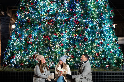 Three adults gathered by the outdoor Christmas tree