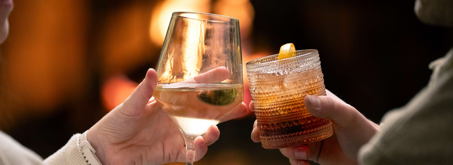 Cheers with two cocktails in front of the glow of the fireplace